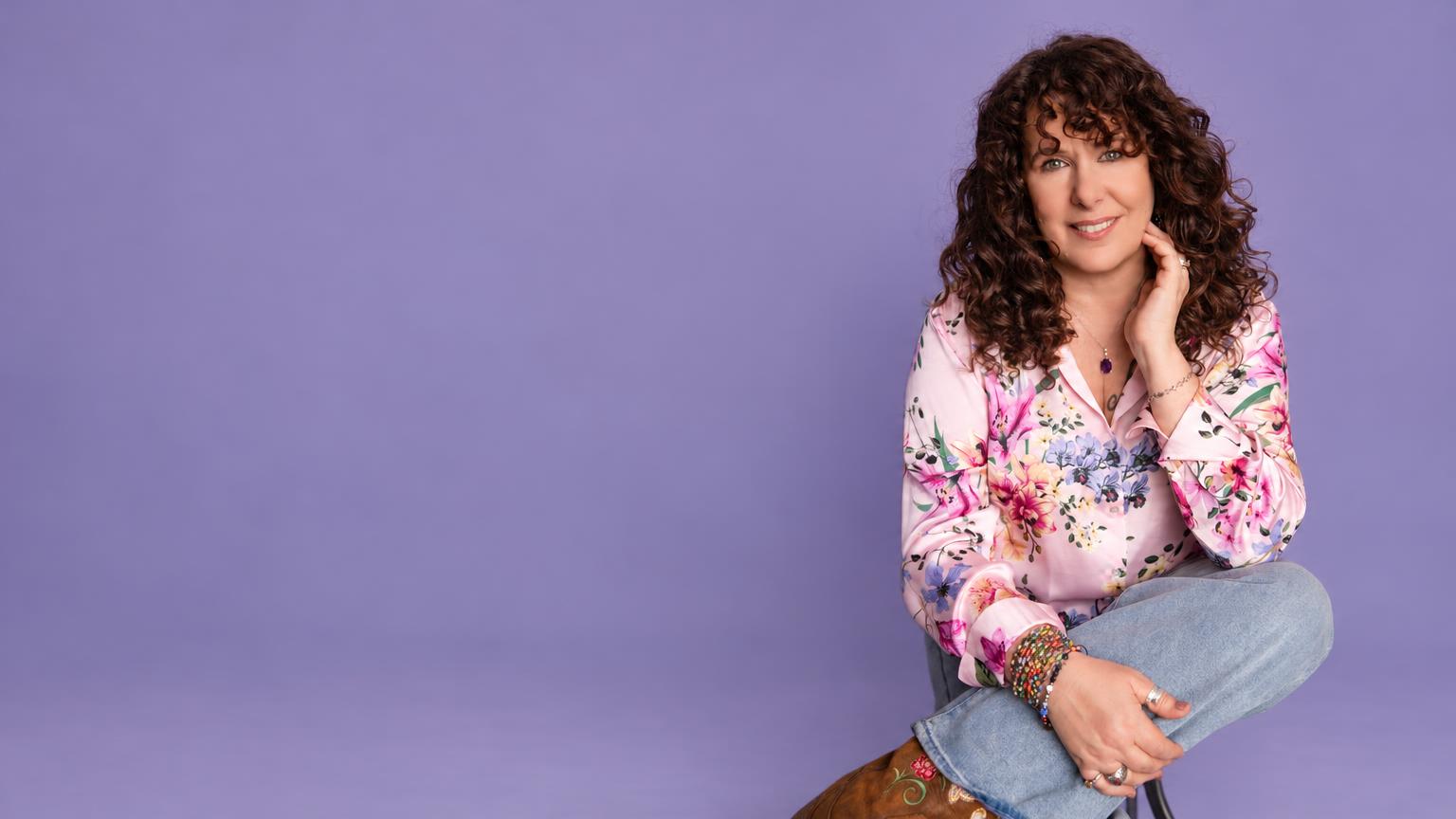 Luannah Victoria Arana seated in a pink floral blouse against a soft lavender studio backdrop